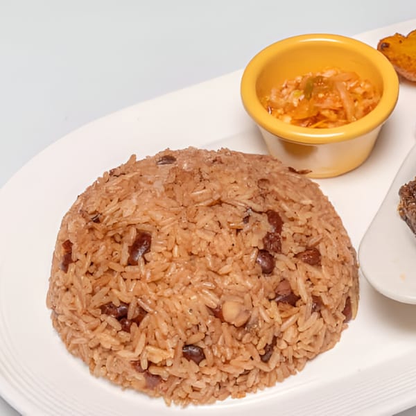 Haitian rice and beans, with a side of pikliz in a yellow ramekin, on a white plate.