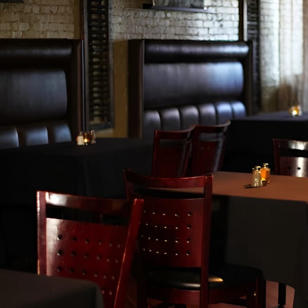 Dimly lit restaurant interior with dark booths, tables with black tablecloths, and red wooden chairs.