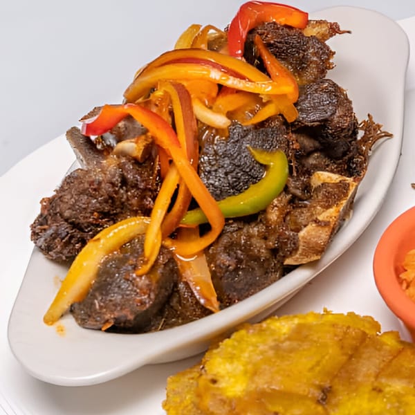 Haitian griot, fried pork shoulder, topped with colorful bell peppers and onions, served with fried plantains.