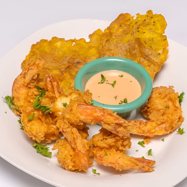 Crispy fried shrimp and a large tostone, with a side of dipping sauce, garnished with parsley.