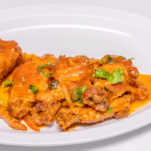 Haitian chicken wings coated in a rich orange sauce and garnished with fresh parsley on a white plate.