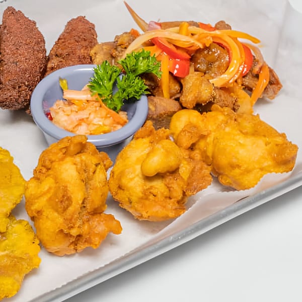 Haitian griot, fried plantains, accra, and pikliz served on a white tray.